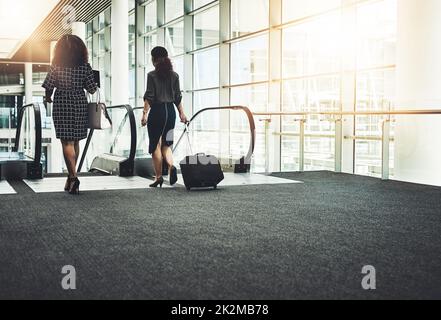 You gotta go where business calls. Rearview shot of two unrecognizable businesswomen going on an escalator in a modern workplace. Stock Photo