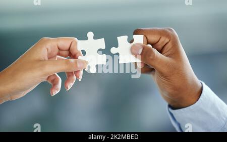 Putting the pieces together. Cropped shot of two unrecognizable businesspeople fitting puzzle pieces together while standing in their office. Stock Photo