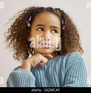 Hang on, I need to think about it. Shot of an adorable little girl standing alone and looking contemplative. Stock Photo