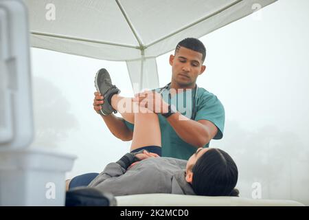 How does that feel. Cropped shot of a handsome young male physiotherapist working on a female patient outside. Stock Photo