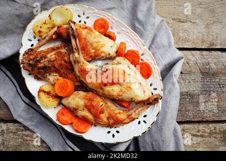 Roasted Rabbit Haunches on white plate with Stewed Vegetables on Rustic Wooden Table Surface Stock Photo