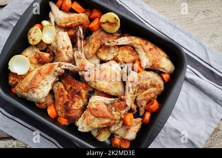 Roasted Rabbit Haunches in Pan with Stewed Vegetables on Rustic Wooden Table Surface Stock Photo