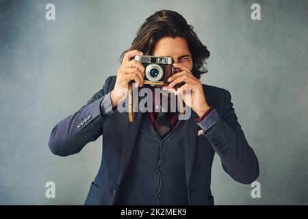 Hes got you framed. Studio shot of a stylishly dressed handsome young man taking a picture with a vintage camera. Stock Photo