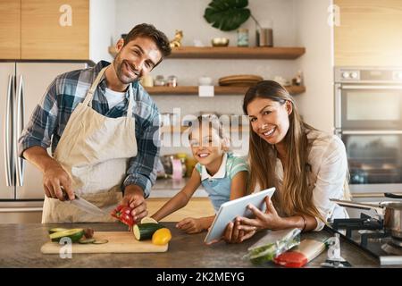 This is how we spend our Saturdays. Portrait of two happy parents and their young daughter trying a new recipe in the kitchen together. Stock Photo