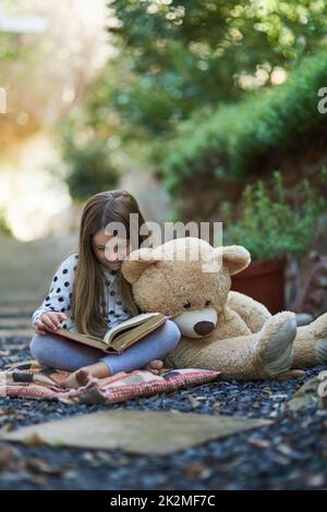 Teddy seems to be taking a nap from storytime. Shot of a little girl reading a book with her teddy bear beside her. Stock Photo