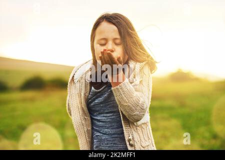 Sending her love long-distance. Portrait of a sweet little girl blowing a kiss while standing outside. Stock Photo