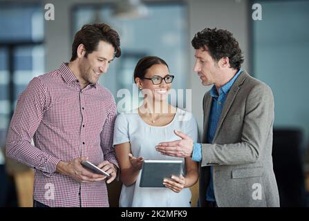 Putting their plans into action. a group of coworkers standing in an office talking over a digital tablet. Stock Photo