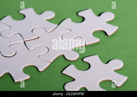 Close-up on jigsaw puzzle pieces, blank white paper jigsaw puzzle elements linked together and separate. Closeup shot on green paper. Stock Photo