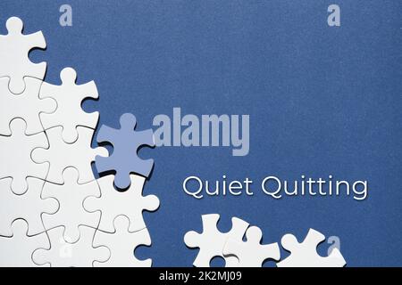 Quiet quitting text, caption. Jigsaw puzzle pieces half assembled and separate.Top view, flat lay, blue white paper background. Stock Photo