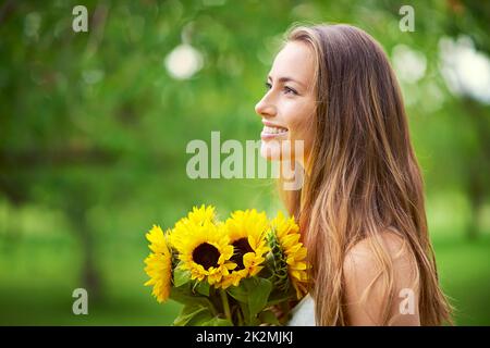 Be like a sunflower, turn your face to the sun. Shot of a young woman holding a bunch of sunflowers outside. Stock Photo