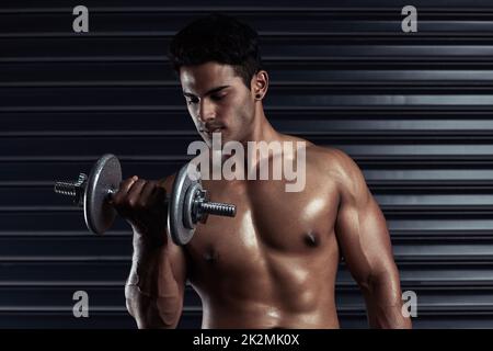 Building his body. Cropped shot of an athletic young man working out with a dumbbell. Stock Photo