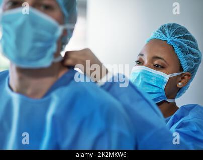 Safety is critical in every medical procedure. Shot of surgeons putting on protective clothing in preparation for a surgery. Stock Photo