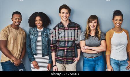 Good friends stand together. Studio portrait of a diverse group of young people standing together against a gray background. Stock Photo