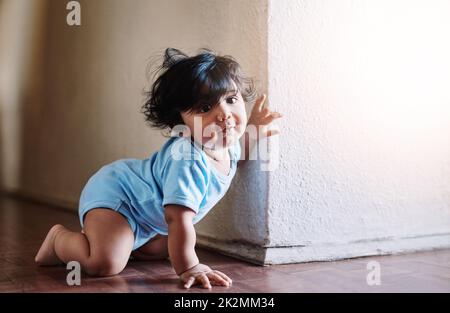 Looks whos around the corner. Shot of a little baby boy playing and hiding around a corner at home during the day. Stock Photo