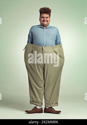 Diet progress. Shot of an overweight man wearing a pair of oversized pants looking pleased. Stock Photo