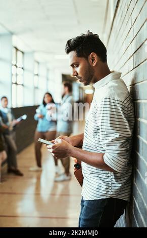 Adding his exams to his calendar. Cropped shot of a handsome young male university student using his cellphone while standing in a campus corridor. Stock Photo