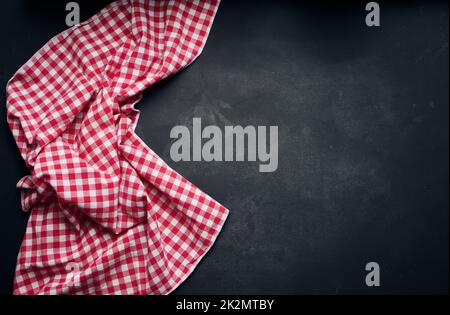 Folded red and white cotton kitchen napkin on a wooden black background, top view, copy space Stock Photo