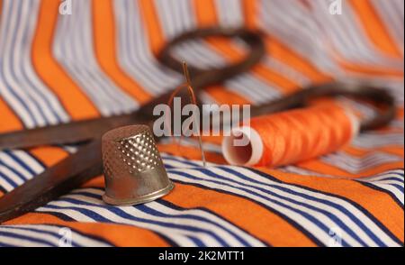 Orange Thread and Thimble on Orange and White Striped Fabric Stock Photo