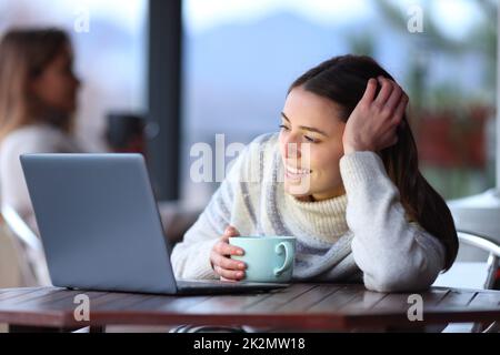 Happy woman in winter watching media on laptop in a bar Stock Photo