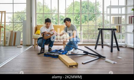 Two asian carpenters installing wooden bench in new house. House renovation service. Morning work atmosphere in the living room. Stock Photo