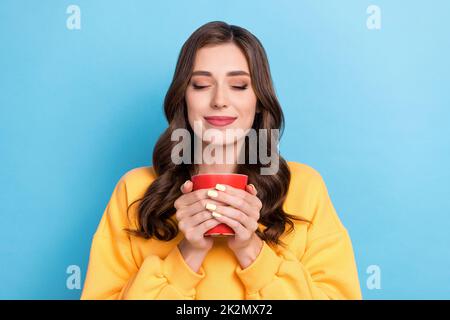 Photo portrait of gorgeous young girl smell enjoy coffee aroma closed eyes dressed stylish yellow garment isolated on blue color background Stock Photo