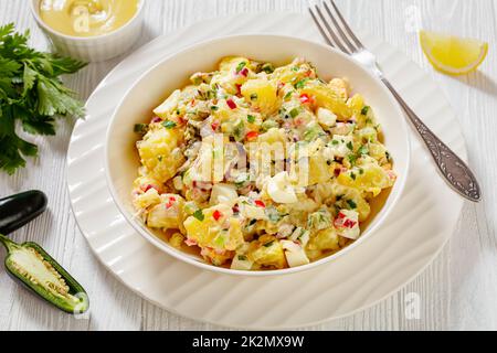 hallelujah potato salad with pickles, celery, eggs, jalapeno and mayonnaise dressing in white bowl on wooden table, landscape view Stock Photo