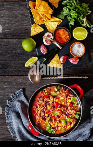 taco soup of ground beef, tomatoes, chopped green chilis, onions, corn, red beans and taco seasoning in red pot on wood table, vertical view Stock Photo