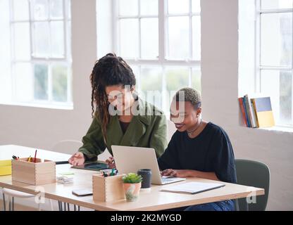 College students working together two young women friends brainstorming ideas for project sitting at desk using laptop computer in class Stock Photo