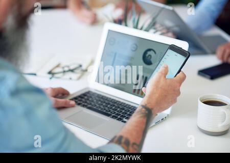businessman using smartphone working on laptop computer with financial graph data on screen Stock Photo
