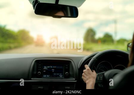 Back view of a woman driving car for summer road trip travel. Car driving with safety on asphalt road. Driver hand holding steering wheel for control car. Inside view of car. Dashboard and windshield. Stock Photo