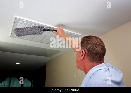 Man Dusting with a Dust Wand a Ceiling Furnace Air Intake Vent Grid Stock Photo