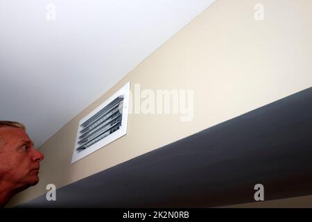 Adult Male Looking Into a Small Rectangle Air Vent on a Wall Stock Photo