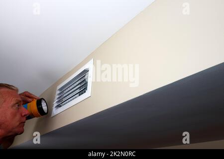 Man Looking into a Rectangle Home Wall Vent with a Flashlight Stock Photo