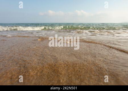 Wet sand on the beach, sea in distance, low angle photo on ground level, lens covered with some drops to emphasise water. Abstract marine background. Stock Photo