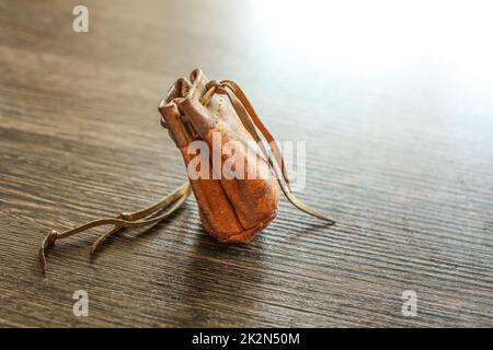 Old worn leather coin pouch on glossy wood desk, white light reflected in background. Stock Photo
