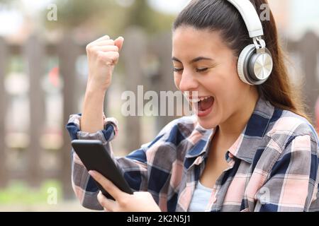 Excited teen with headphones checking smart phone Stock Photo