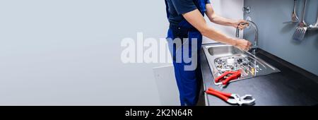 Plumber Fixing Faucet In Kitchen Stock Photo