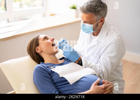 Male Dentist Treating Teeth Of Young Pregnant Woman Stock Photo
