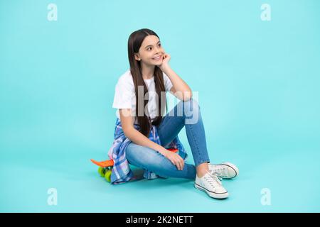 Sporty teenager girl with skateboard. Fashion child in trendy style on blue background. Happy teenager, positive and smiling emotions of teen girl. Stock Photo