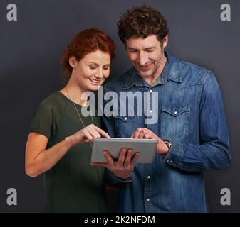 Sharing the same device. a happy young couple using a digital tablet. Stock Photo