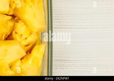 Tabletop view, detail - yellow pineapple cut in pieces, in square glass bowl, white boards desk / space for text on right. Stock Photo