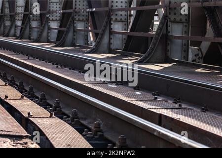 Detail on railway tracks at steel rail bridge lit by sun. Stock Photo