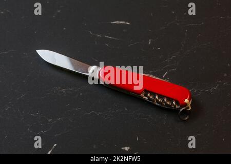 Red pocket knife on black table. Stock Photo