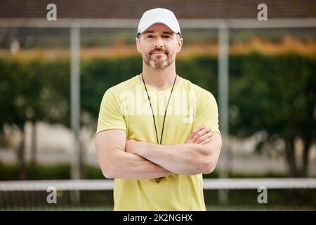 Hes one confident coach. Cropped portrait of a handsome mature male tennis coach standing with his arms folded on the court. Stock Photo
