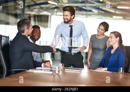 Another fine job in the books. Shot of two colleagues shaking hands while in a meeting with colleagues in a boardroom. Stock Photo