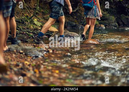 The only thing better than exploring is exploring with friends. Cropped shot of a group of unidentifiable hikers crossing a stream while exploring in the woods. Stock Photo