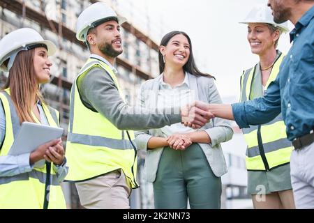 When we strive to become better than we are. Shot of a team of builders shaking hands on a construction site outside. Stock Photo