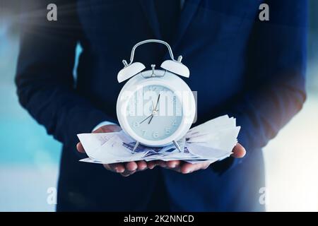 Make the most of your time. Cropped shot of an unrecognisable businessman standing alone in the office and holding an alarm clock. Stock Photo