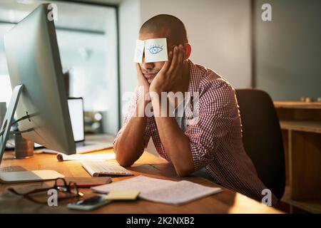 When staying awake is near impossible. Cropped shot of a young designer working late in an office with adhesive notes covering his eyes. Stock Photo
