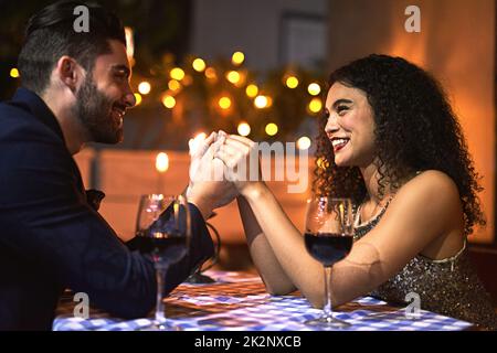 We will stay together forever. Shot of a cheerful young couple holding hands while looking into each others eyes over a candle lit dinner date at night. Stock Photo